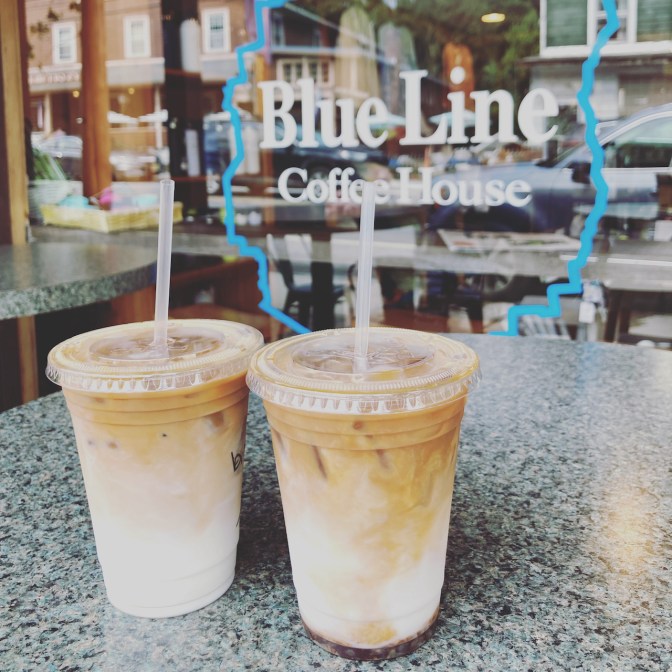 Two lattes on table, with sign on window in background that says BLUE LINE COFFEE HOUSE