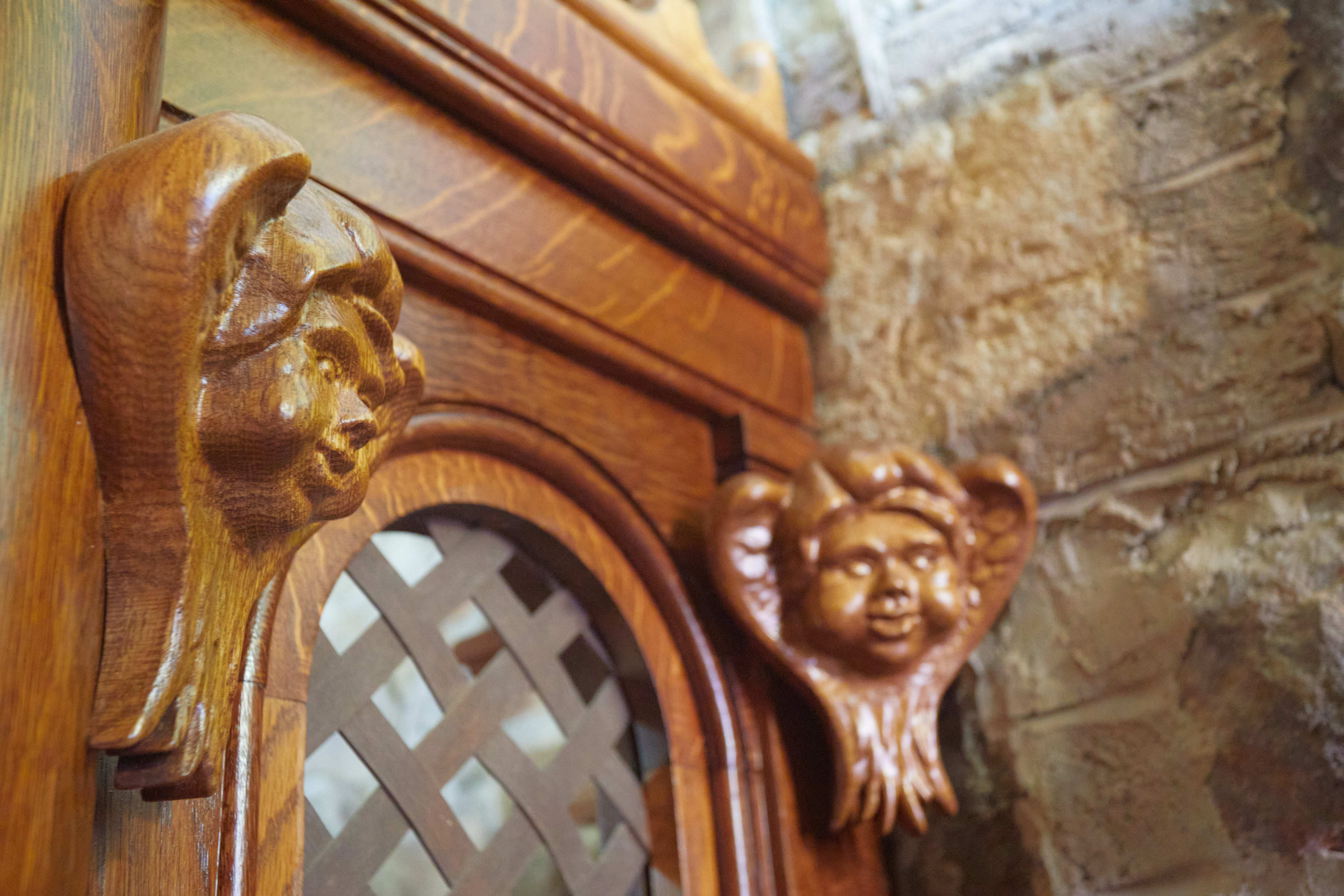 Cherub faces carved into wood on side of confessional.