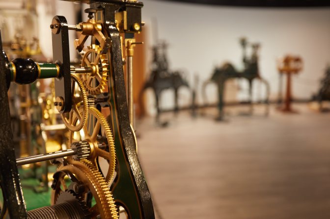 Mechanical interior of clock, with other clocks on display in background.