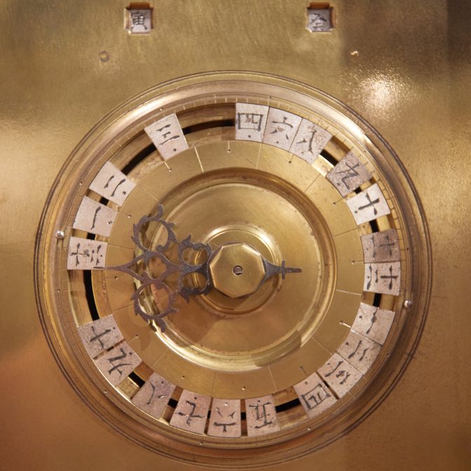 Japanese clock - bronze with writing in Japanese script around clock face.