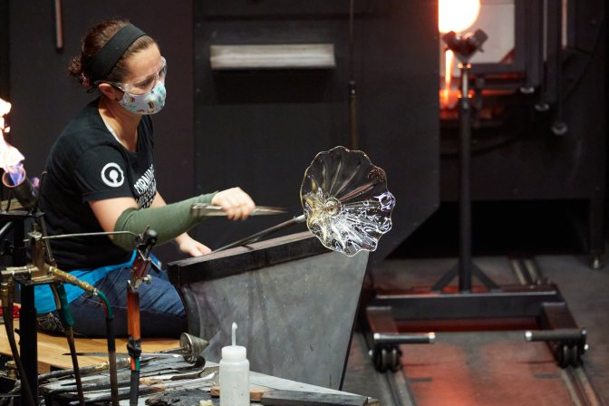 Woman, working with glass bowl on end of blowpipe.