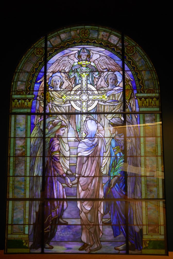 Stained glass window of women and angel surrounding cross.