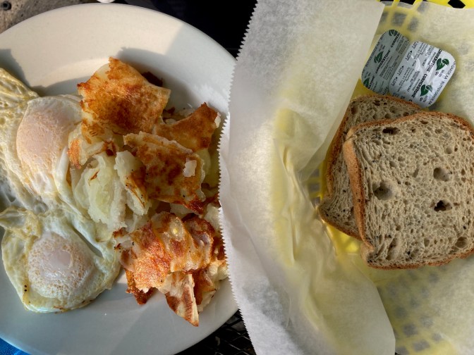 Eggs over easy and home fries on plate, with gluten-free rye bread.