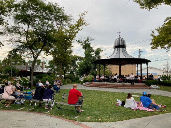 Audience listening to band playing under gazebo in public park.