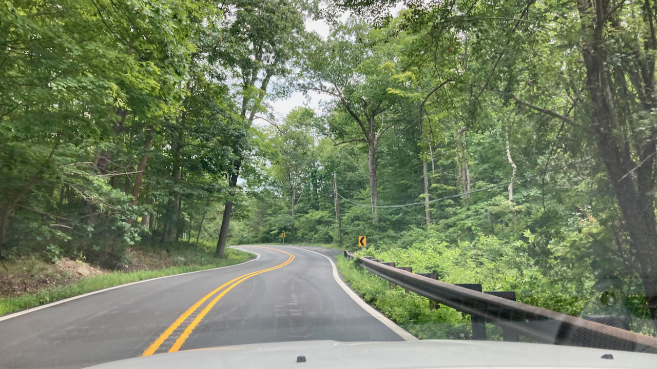 Two-lane road, tree-lined, with a steel guard rail along right side.