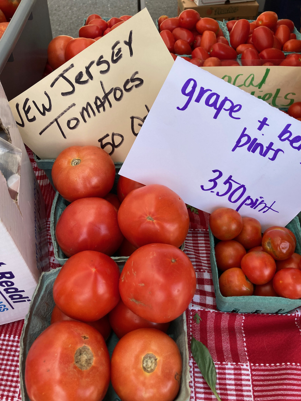 Tomatos on table, with a sign for NEW JERSEY TOMATOES and GRAPE AND BERRY PINTS $3.50 PINT