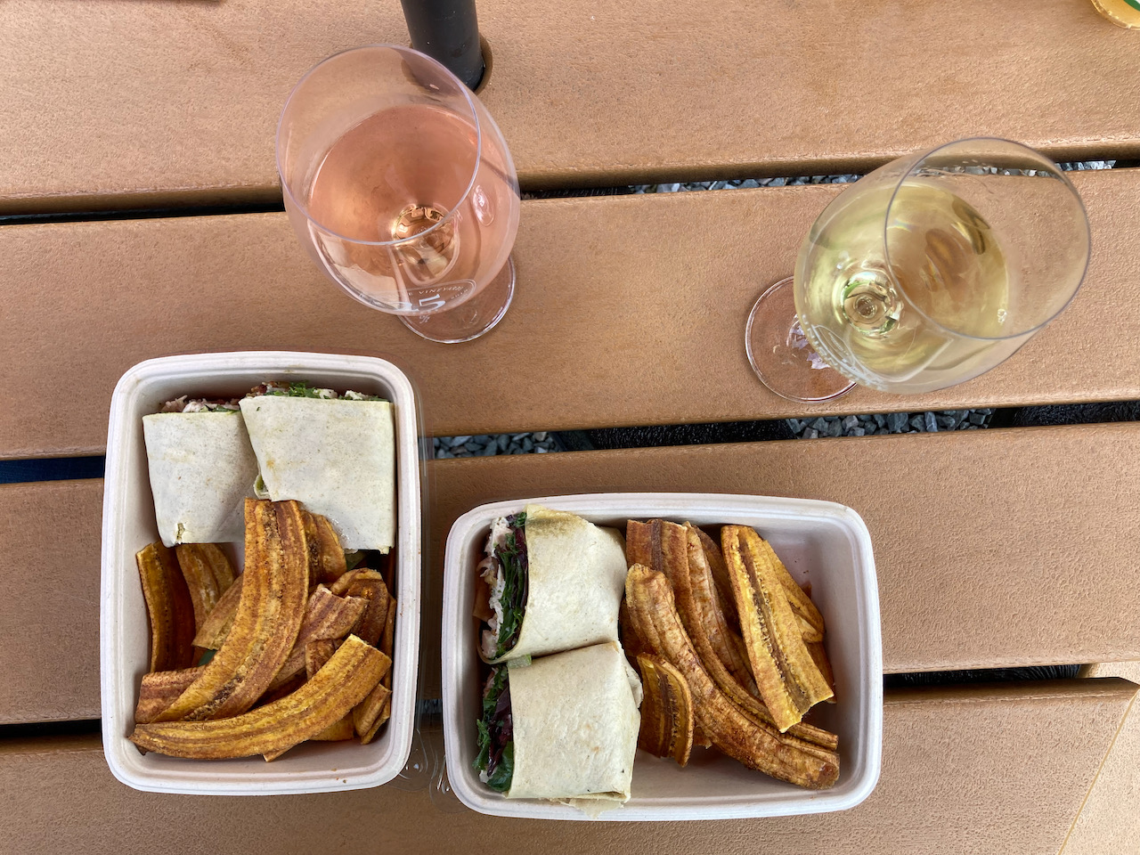 Two glasses of wine, and two to-go containers of sandwich wraps and plantain chips.