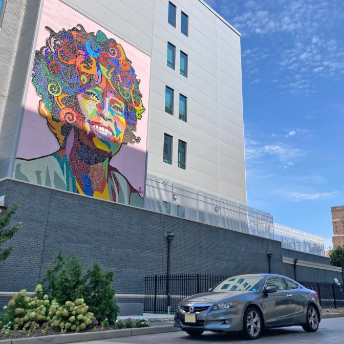 2012 Honda Accord parked beneath mosaic mural of Whitney Houston on side of building.