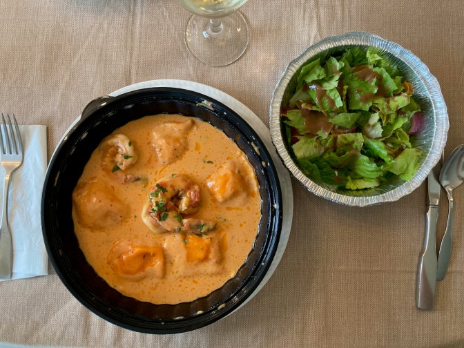 Plate with lobster ravioli, beside bowl with salad.