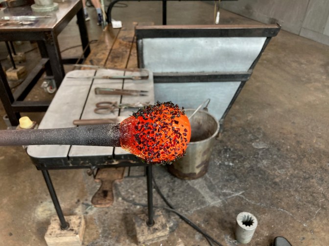Glob of red glass with green glass shard, on metal pole.