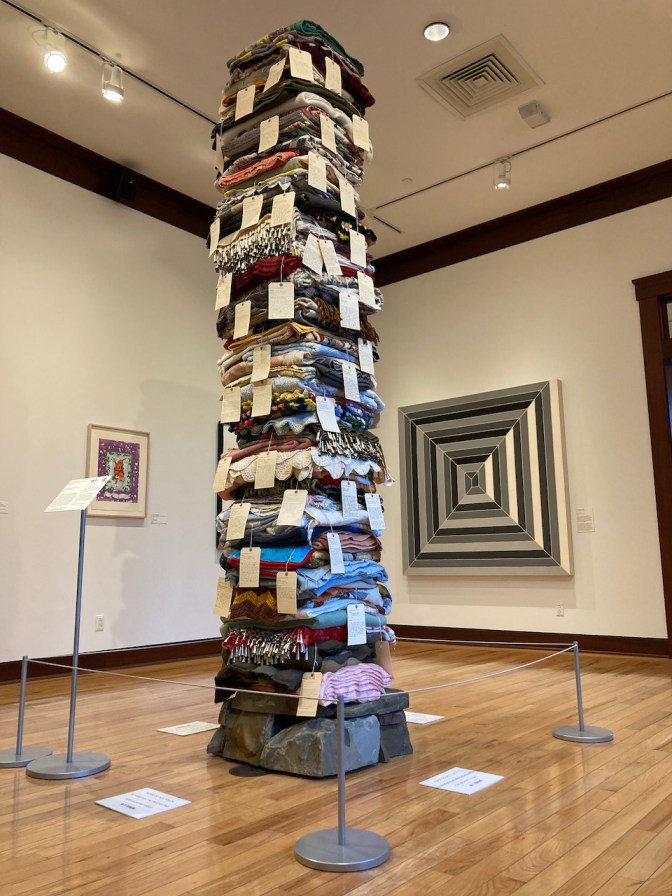 Stack of blankets and quilts in tower, nearly to ceiling.