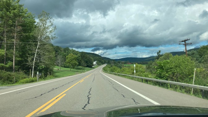 View of twisty road through farmland and mountains.