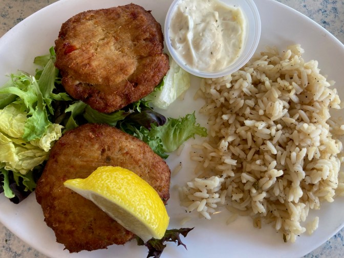 White plate with crab cakes, rice, and tartar sauce.