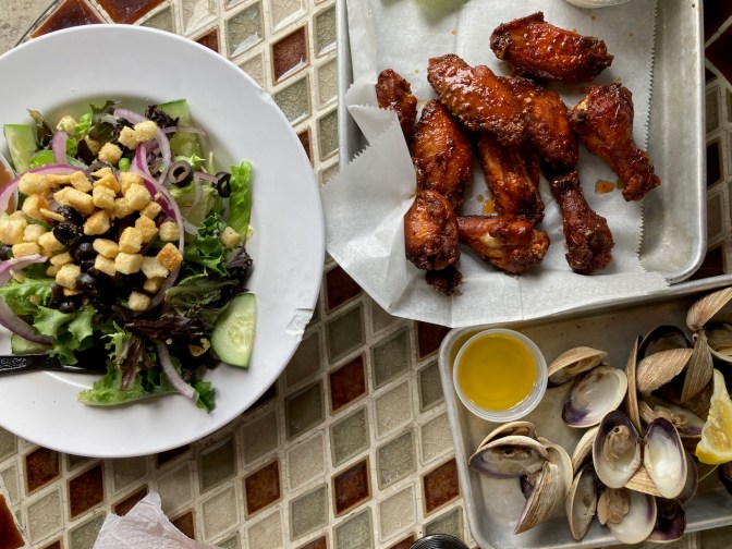 Plate with salad, tray with clams, and tray with chicken wings.