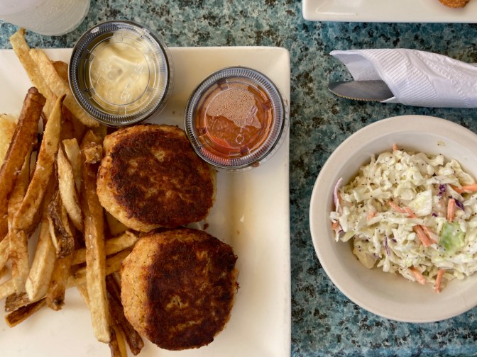 Crab cakes on plate with french fries, alongside a bowl of coleslaw.
