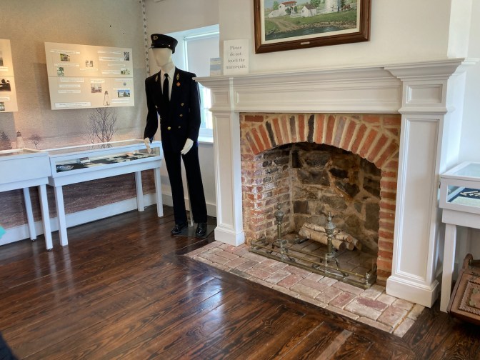 Mannequin dressed as lighthouse keeper, beside fireplace, in museum.