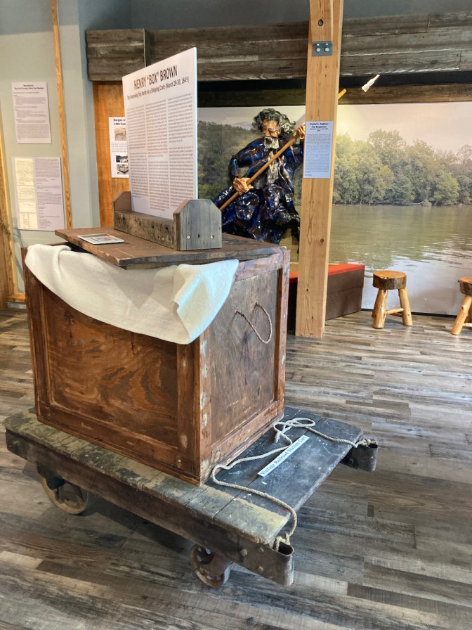 Wooden box, 2' x 2' x 3', with informational placard on top of it.