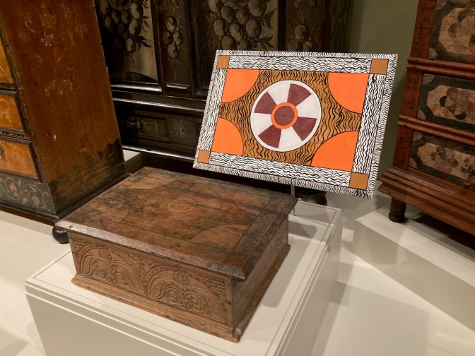 Wooden box, with elaborately painted lid on display beside it.