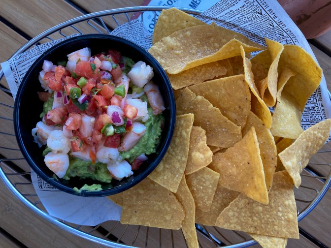 Tortilla chips in basket, with bowl of guacamole and shrimp.