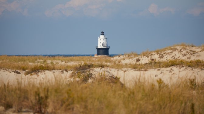 Harbor of Refuge lighthouse, with sand dunes in foreground. 