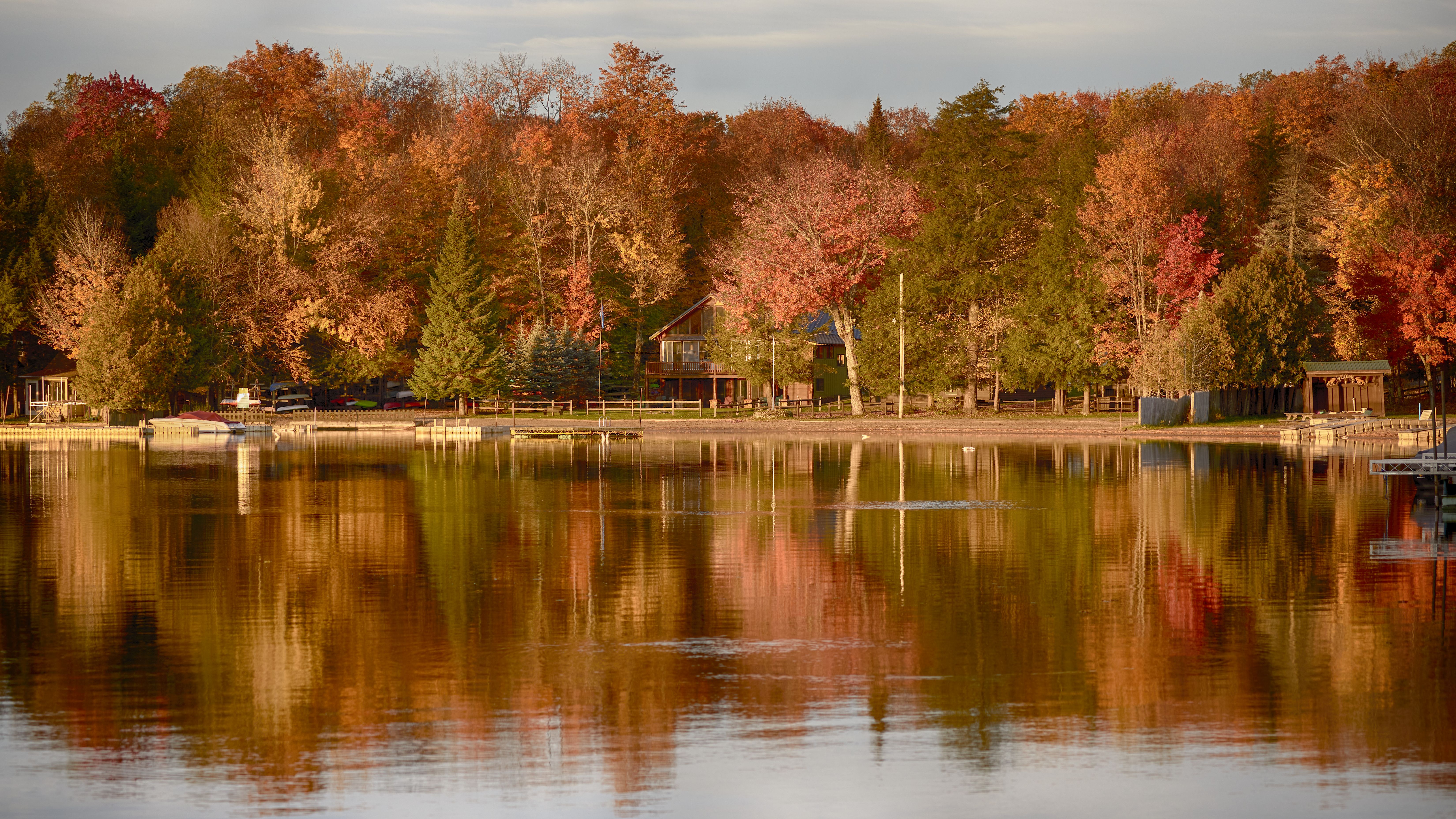 House on lake shoreline, surrounded by colorful trees.