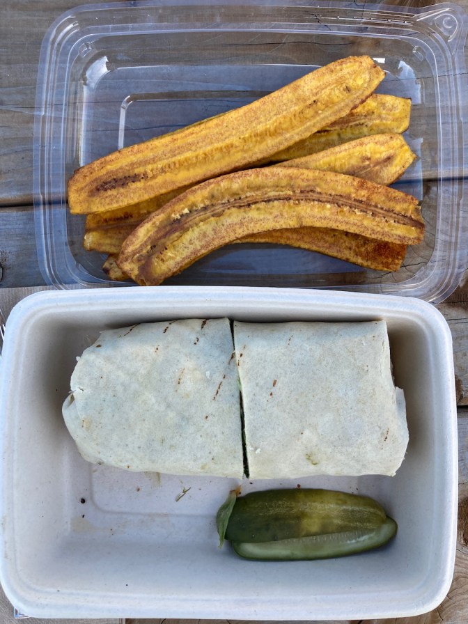 Chicken salad wrap with pickles and plantain chips in plastic container. 
