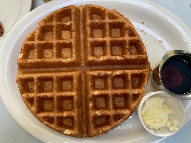 Gluten-free waffle on plate with maple syrup and butter. 