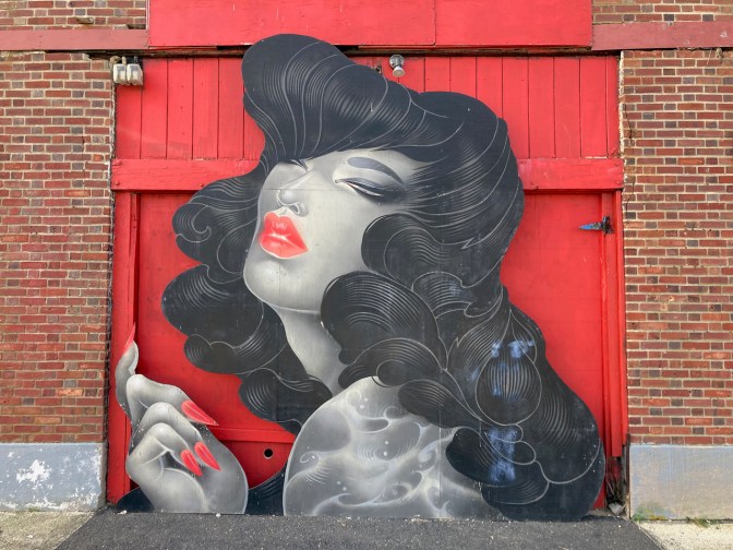Mural of woman in front of brick wall. 