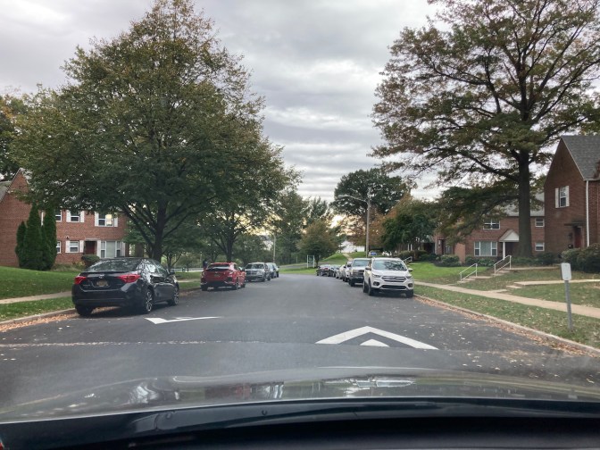 Road through apartment complex, with cars on either side of road.