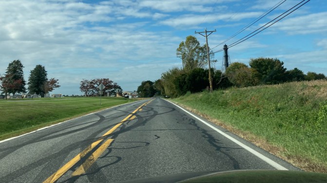 Two-lane road, with steel lighthouse on side of road. 