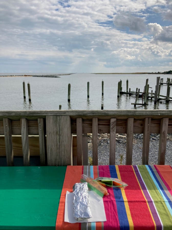 Picnic blanket with food on table, on deck above Christiana River. 