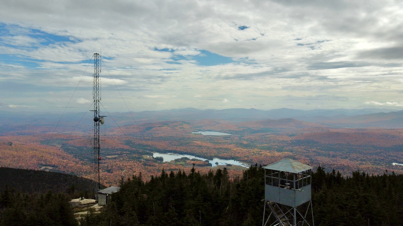 View of fire tower and wireless antenna in foreground, and mountains in background. 