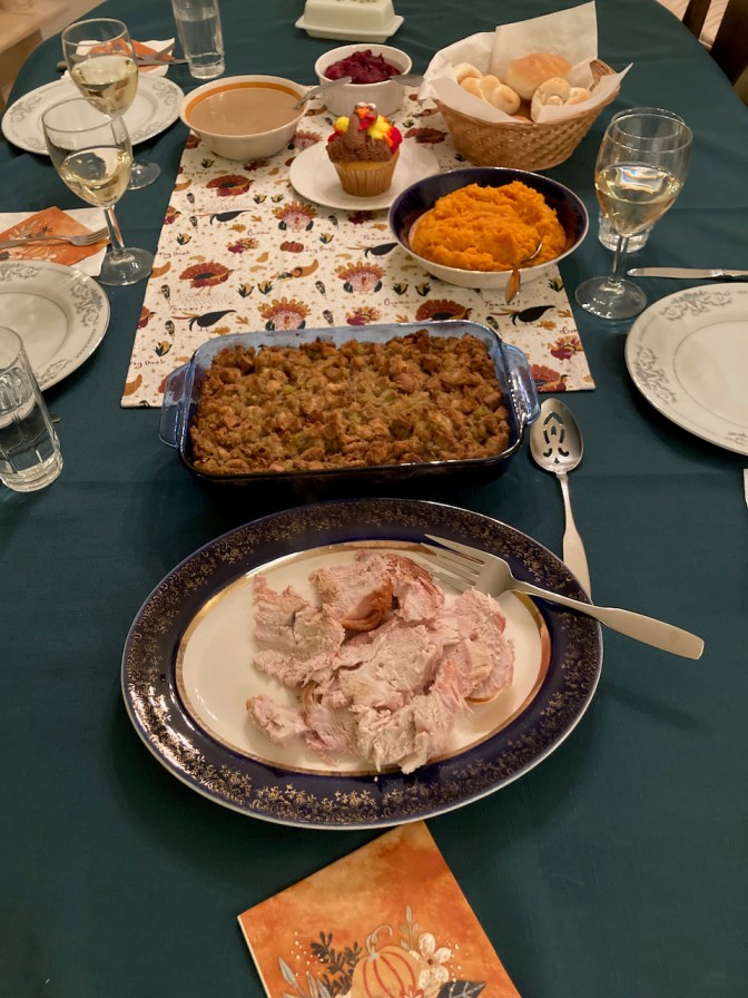 Table with turkey, stuffing, sweet potatoes, rolls, cranberry sauce, gravy, and a turkey cupcake. 