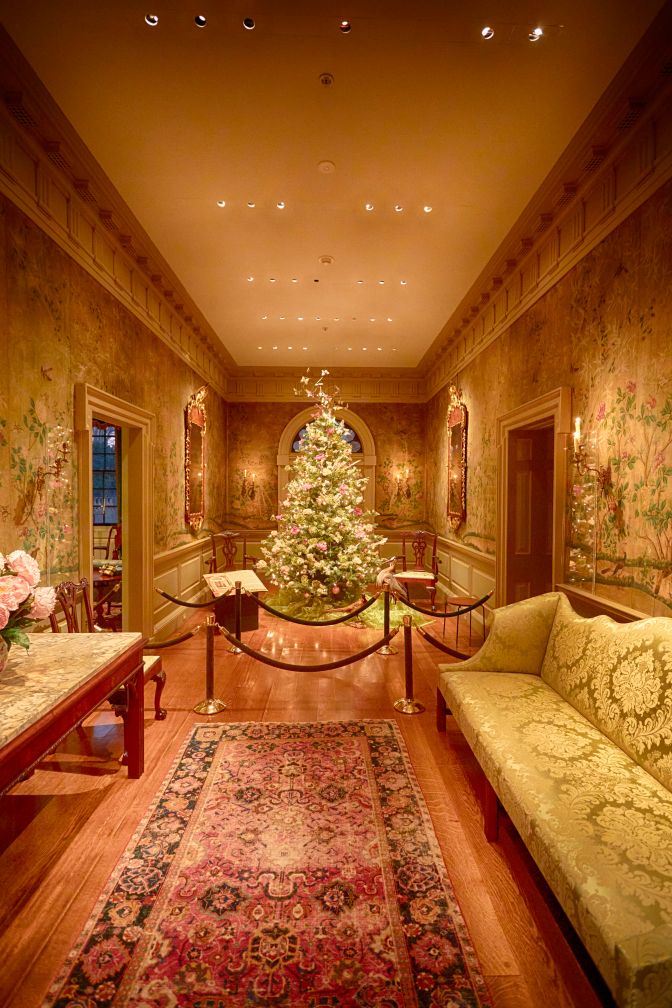 Room with Christmas tree against far back wall, sofa on right side of wall, and table on left wall. 