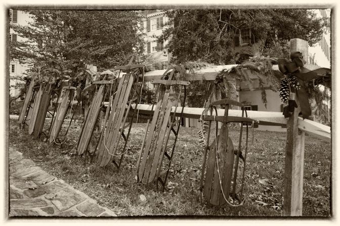 Sleds lined up against wooden fence outside of Winterthur museum.