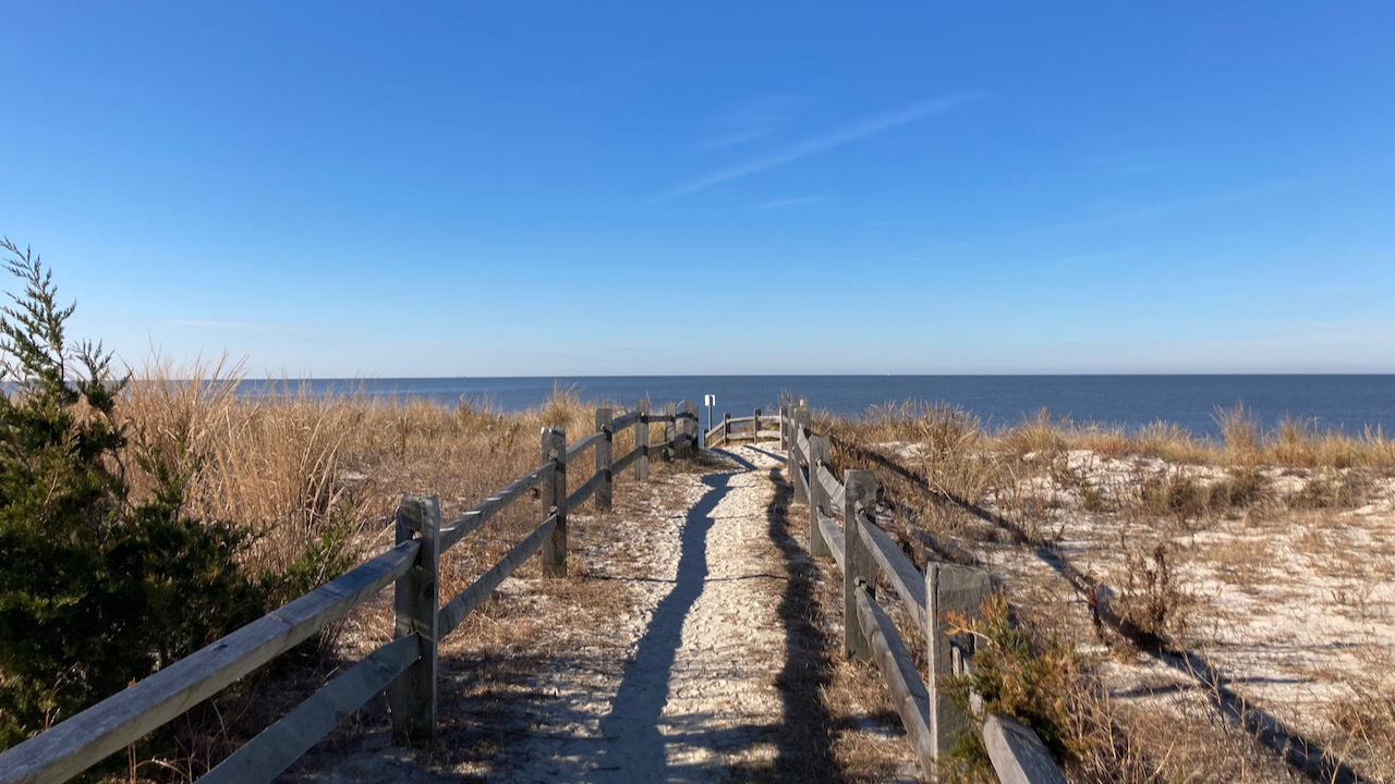 View of beach, with passing cross dunes, leading to sea.