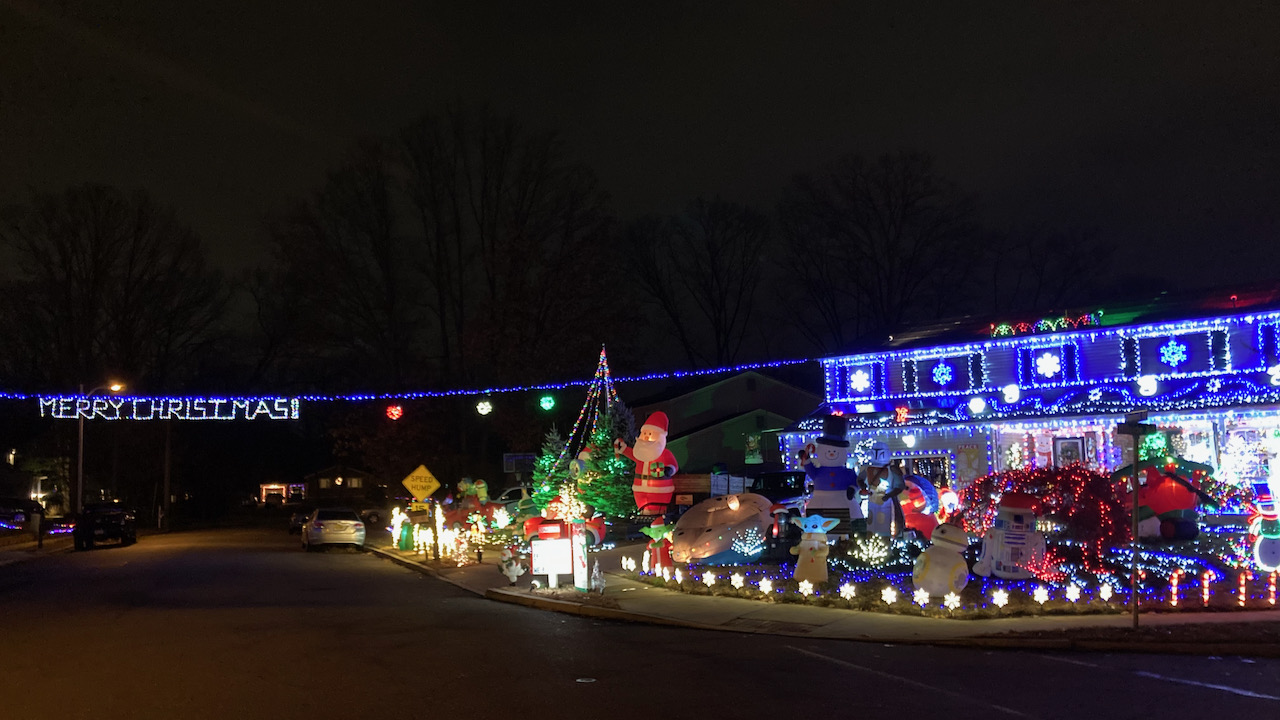 House covered in Christmas decorations, with words MERRY CHRISTMAS strung across roadway.