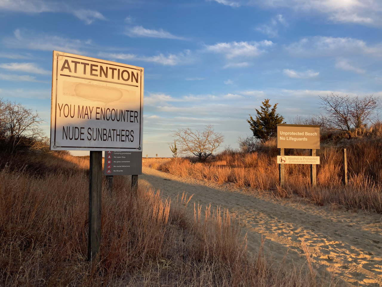 Beach entrance with sign that says ATTENTION YOU MAY ENCOUNTER NUDE SUNBATHERS.