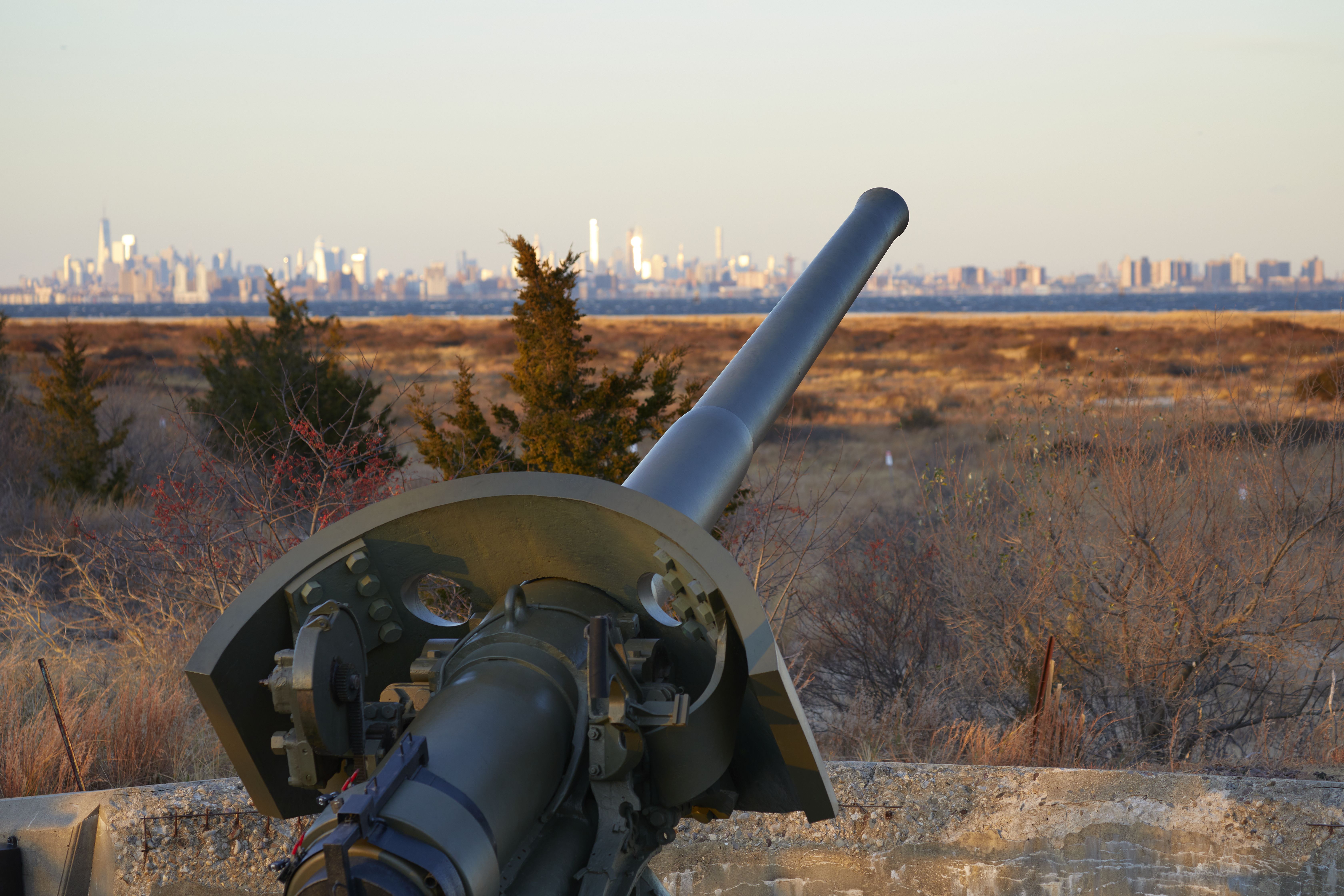 6" gun in foreground, with New York skyline in background.