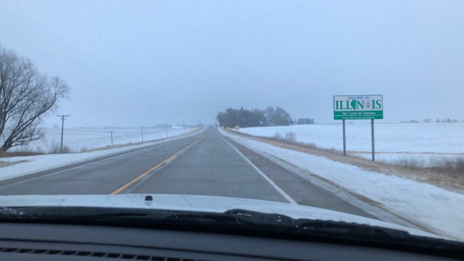 Illinois state line sign beside road.