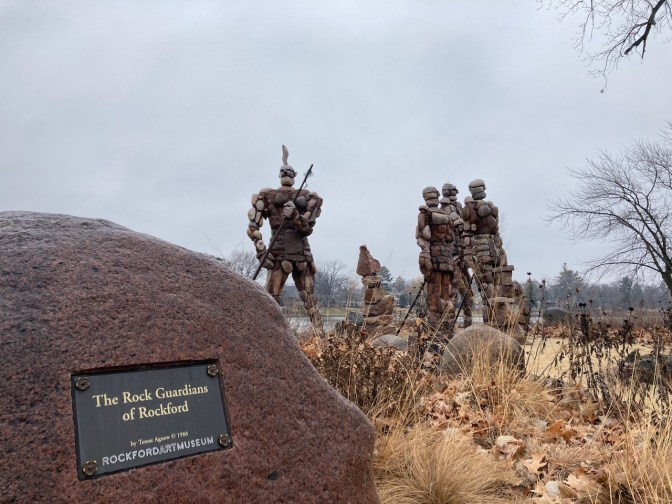 Rock statues of people, with sign in foreground that says ROCK GUARDIANS OF ROCKFORD.