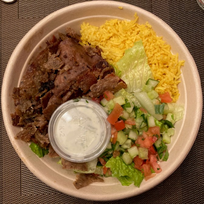 Gyro platter, including rice, beef, and vegetables, in round bowl on plate.