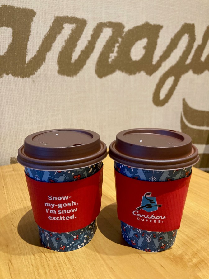 Two paper cups of Caribou Coffee on wooden table.