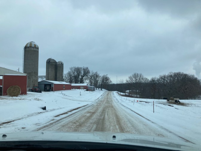 Two-lane, snow-covered road with farm on left side.