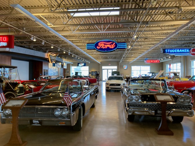 Showroom of classic cars, with neon signage hanging from ceiling.