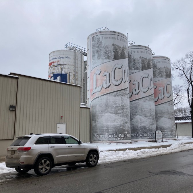 2014 Jeep Grand Cherokee parked in front of two-story tall six pack of beer.