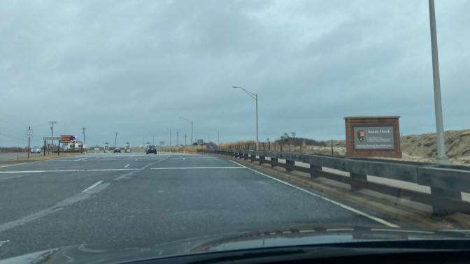 Entrance to Gateway National Recreation Area - Sandy Hook, with a few cars passing through the entrance gate.