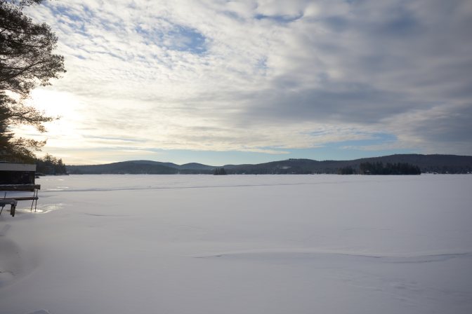 Fourth Lake, covered in snow, under a blue and cloudy sky.
