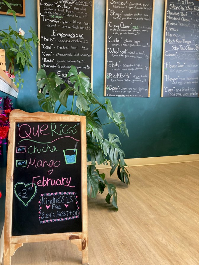 Interior of Que Ricas, with chalkboard menus on wall and on sandwich board on floor.