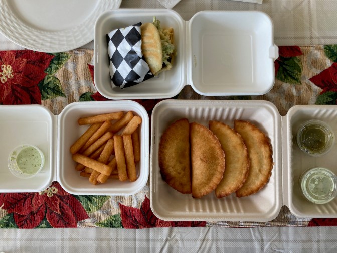 Containers on table, with an arepa, empanadas, and yucca fries.